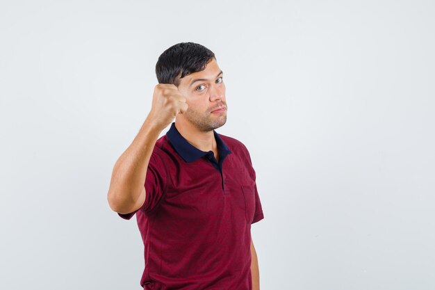 Young man in t-shirt showing raised fist and looking strong , front view.