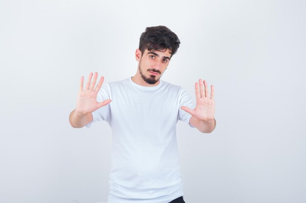 Молодой человек в футболке показывает жест стоп и выглядит испуганным