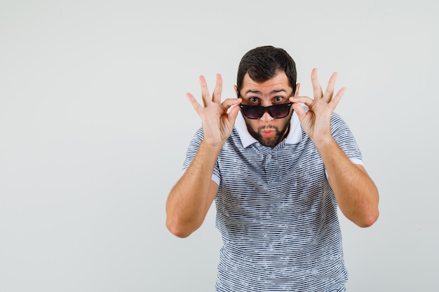 Free photo young man in t-shirt taking off glasses to see clearly and looking surprised