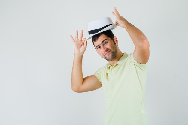 Young man in t-shirt taking off hat and looking confident