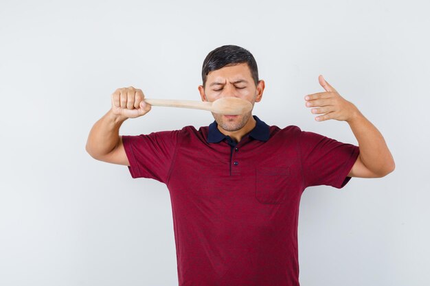 Young man in t-shirt tasting meal with wooden spoon , front view.