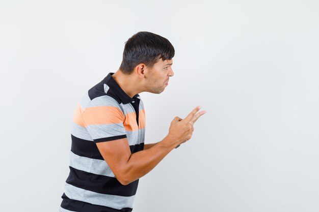 Young man in t-shirt warning somebody with fingers and looking angry 