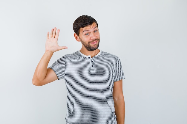 Foto gratuita giovane in t-shirt agitando la mano per salutare e sembrare allegro, vista frontale.