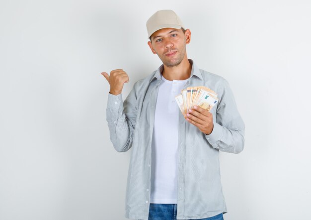 Молодой человек в футболке с кепкой, джинсы указывая в сторону с деньгами