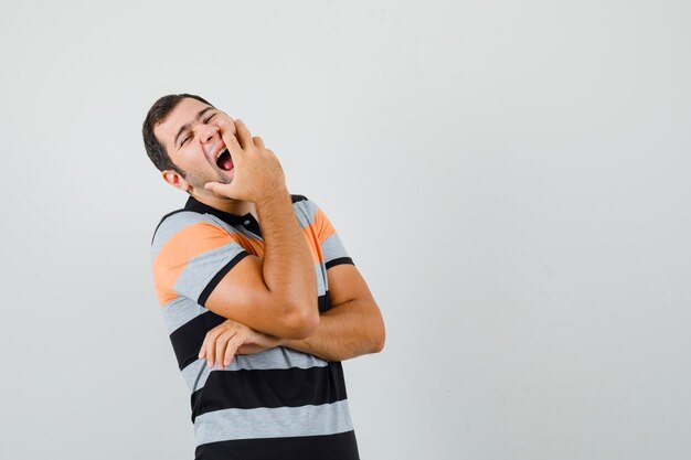 Young man in t-shirt yawning with hand on mouth and looking sleepy space for text