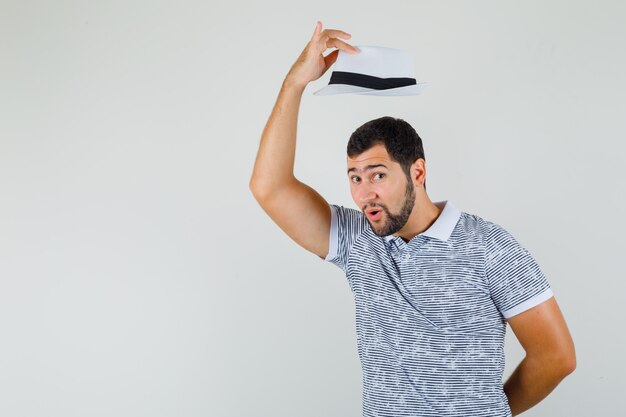 Young man take off his hat with respect in striped t-shirt,hat and looking focused. front view.