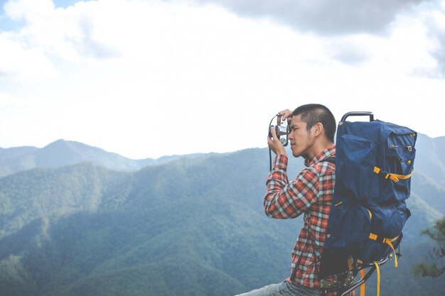 A young man takes pictures of mountain peaks in a tropical forest along with backpacks in the forest. Adventure, travel, hiking.