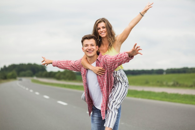 Foto gratuita giovane che cattura la sua ragazza sulle spalle giro sulla strada di campagna