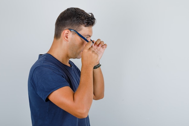 Young man taking off glasses in dark blue t-shirt and looking tired .