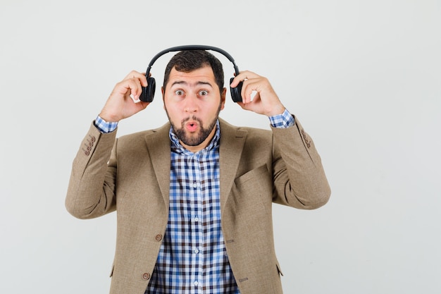 Free photo young man taking off headphones in shirt, jacket and looking wondered