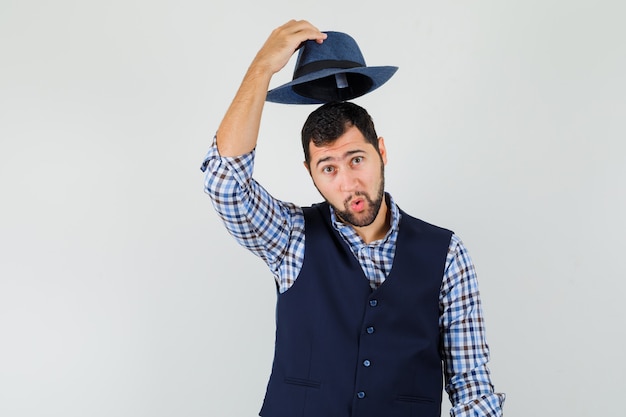 Young man taking off his hat in shirt, vest and looking handsome