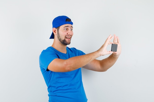 Young man taking photo on mobile phone in blue t-shirt and cap and looking cheerful