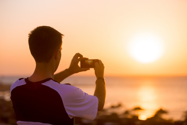 若い男は、写真を撮って、海の夕日