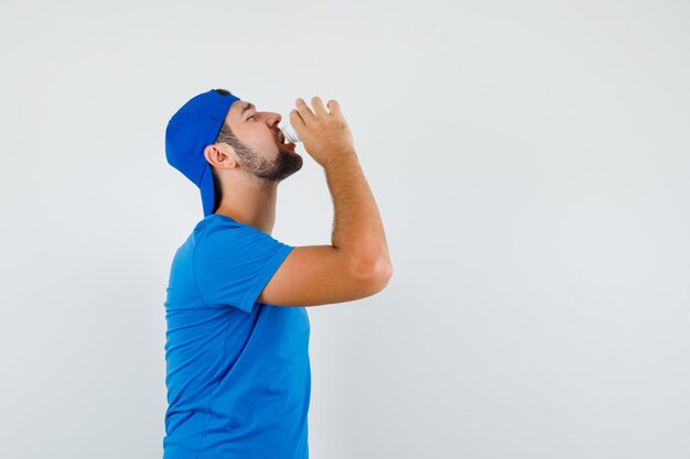 Young man taking pills in blue t-shirt and cap and looking distressed. .