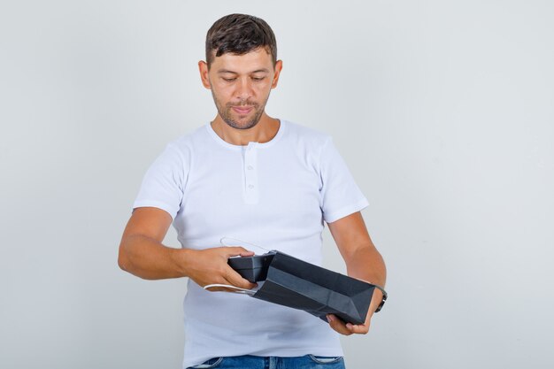 Young man taking present box out of bag in white t-shirt, jeans front view.