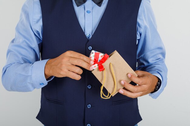 Young man taking present out of paper bag in suit 