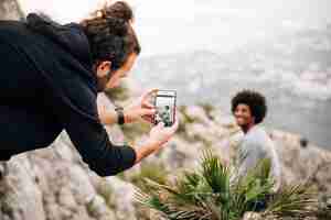 Free photo young man taking selfie of his friend sitting on the mountain