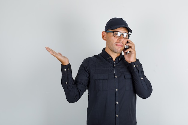 Young man talking on mobile phone in black shirt with cap, glasses