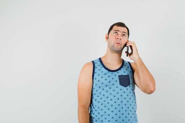 Young man talking on mobile phone in blue singlet and looking pensive , front view.