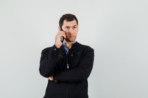 Young man talking on mobile phone in shirt, jacket and looking pensive , front view.