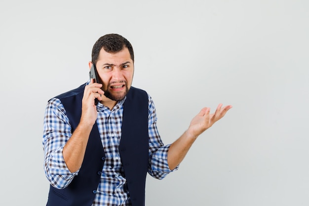 Young man talking on mobile phone in shirt, vest and looking furious