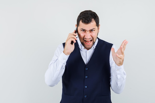 Young man talking on mobile phone in shirt and vest and looking nervous