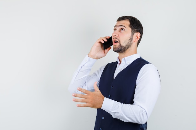 Young man talking on mobile phone in shirt and vest and looking pensive