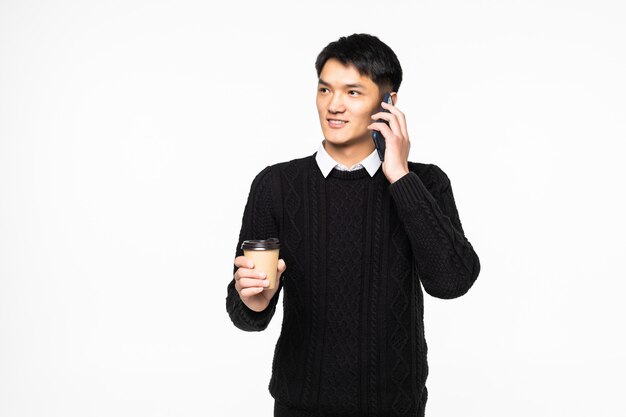 Young man talking on mobile phone with coffee on white wall