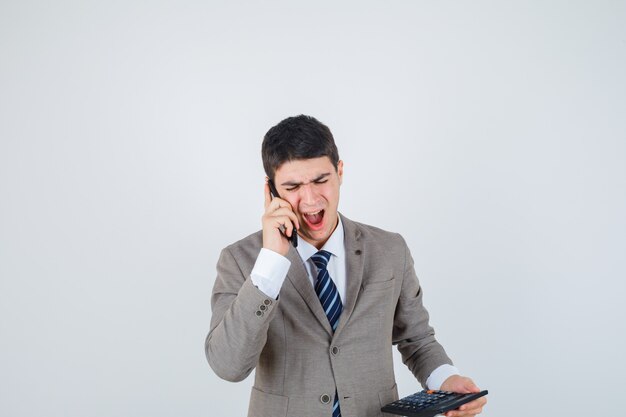 Young man talking to phone, holding calculator in formal suit