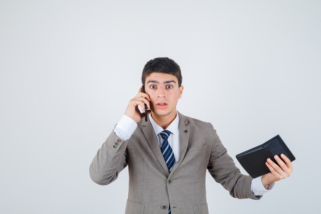 Young man talking to phone, holding calculator in formal suit