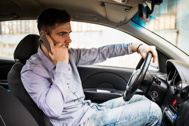 Молодой человек разговаривает по телефону за рулем своего автомобиля