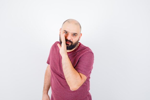 Young man talking secretly in pink t-shirt and looking focused , front view.