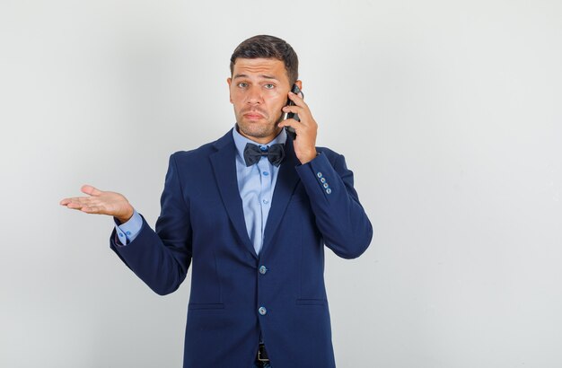 Young man talking on smartphone in suit and looking helpless 