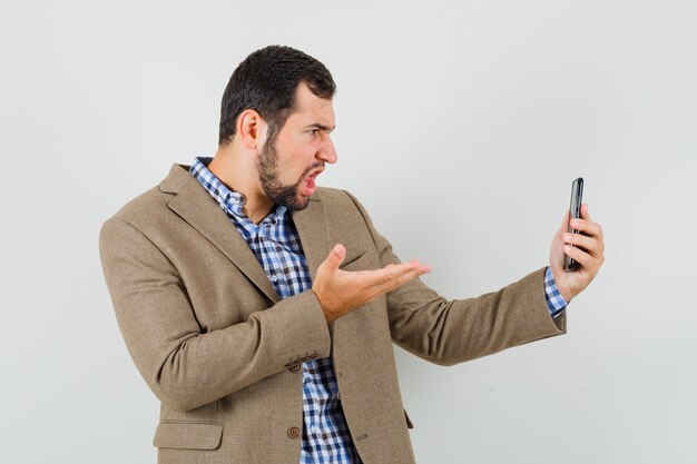 Young man talking on video chat in shirt, jacket and looking angry