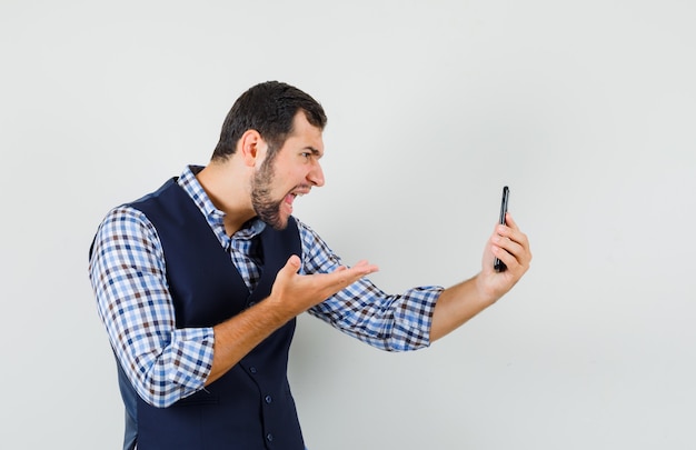 Giovane che parla in chat video in camicia, canotta e sembra arrabbiato