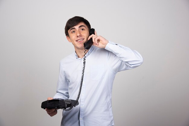 Young man talking with someone via landline phone on gray wall.