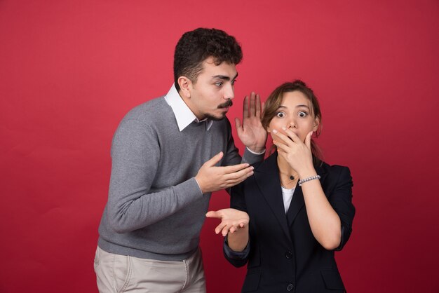 Young man tells some rumors to his girlfriend on red wall