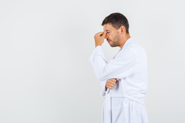 Young man thinking with closed eyes in white bathrobe.