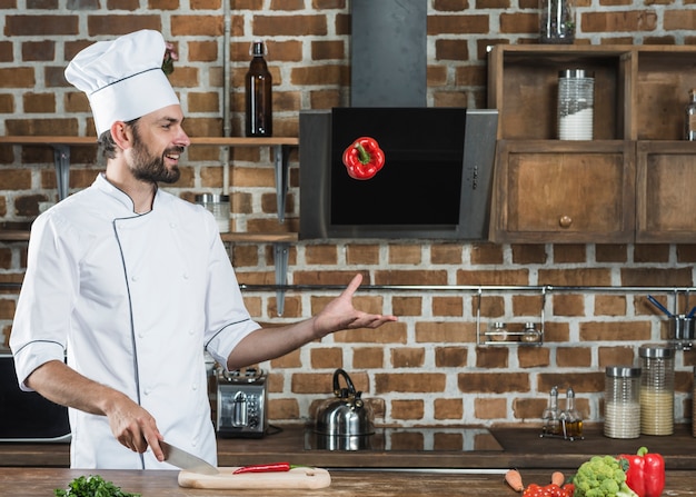 Young man throwing red bell pepper while cutting red chili on chopping board