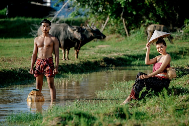 Young man topless standing and holding bamboo fishing trap  to catgh fish for cooking with beautiful woman sitting near swamp