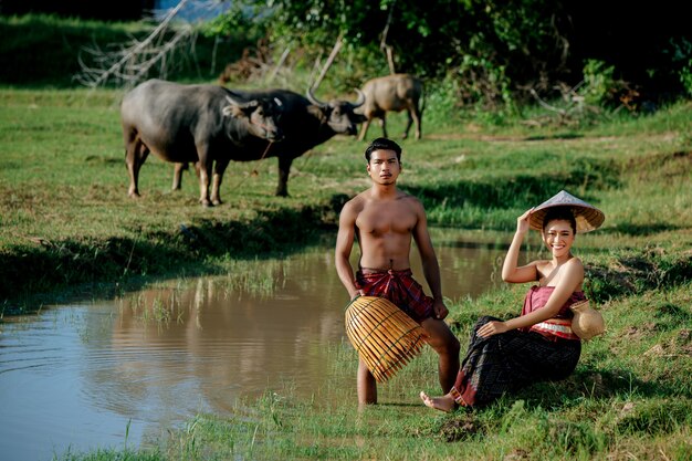 젊은 남자 토플리스 서서 늪 근처에 앉아있는 아름다운 여성과 함께 요리를 위해 물고기를 잡기 위해 대나무 낚시 덫을 들고
