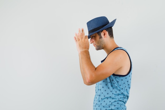 Young man touching hat with fingers in blue singlet and looking handsome. .