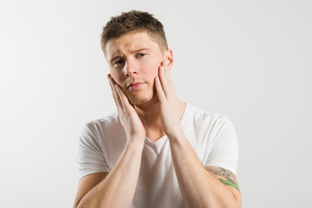 Young man touching his cheeks with two hands against white background