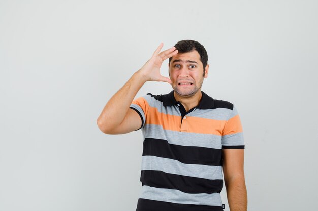 Young man touching his face with hand in t-shirt and looking anxious , front view.