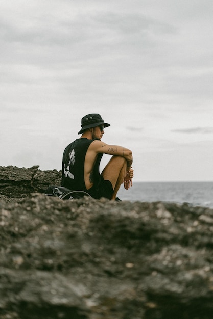 A young man traveler with a backpack on the ocean on the rocks looks into the distance.