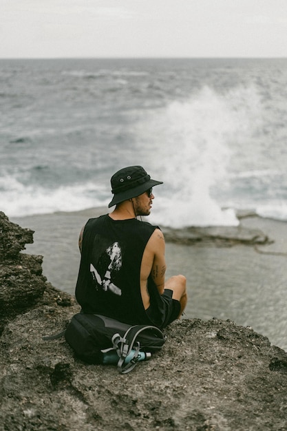 A young man traveler with a backpack on the ocean on the rocks looks into the distance.