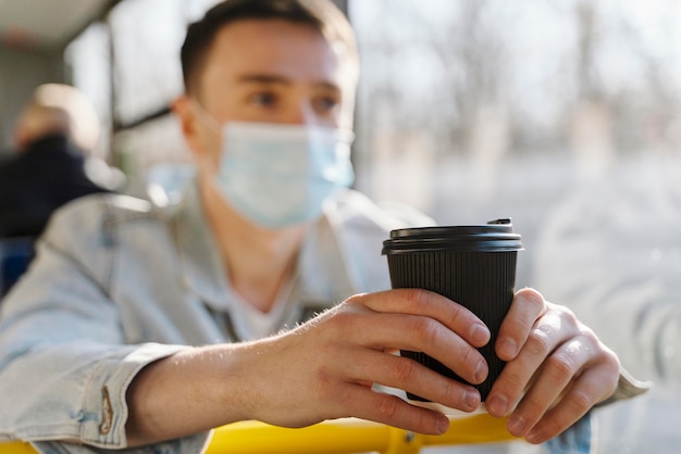 Young man travelling by city bus holding a coffee cup