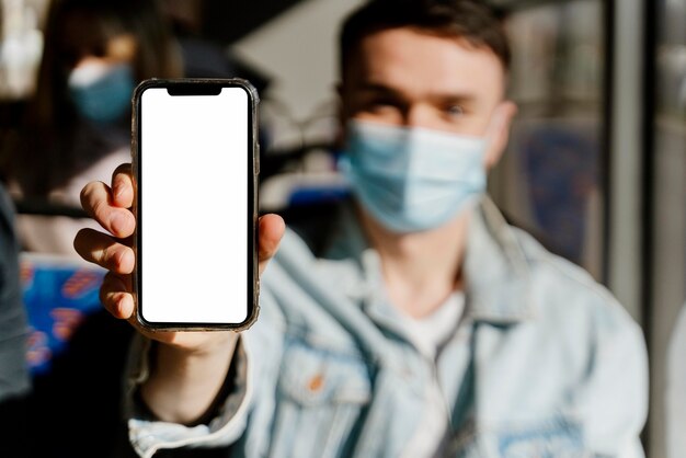 Young man travelling by city bus showing smartphone with blank screen