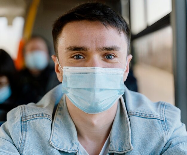 Young man travelling by city bus wearing surgical mask