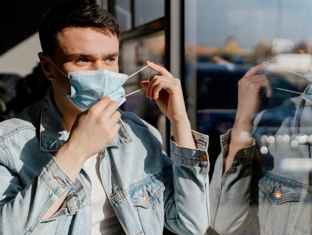 Free photo young man travelling by city bus wearing surgical mask